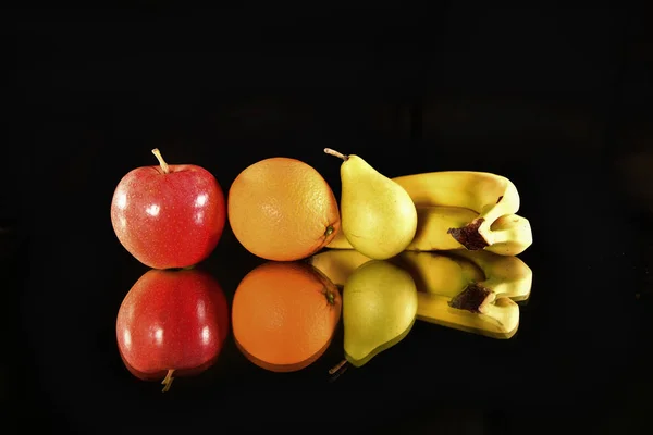 Fresh fruits on black background with reflection. Apple, orange, pear and banana