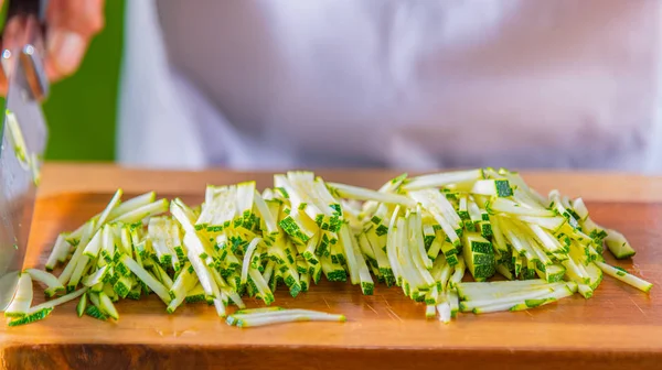 Şef mutfakta ahşap tahta üzerinde ince dilimler halinde yeşil kabak kesme, Close-Up — Stok fotoğraf