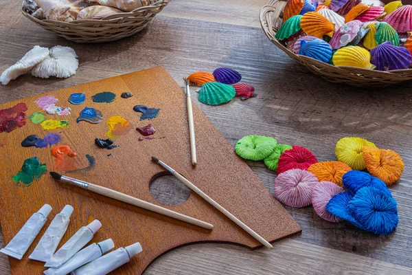 Painted sea shells. Color pallet with paint brush on a wooden table.