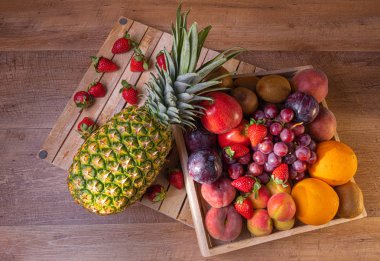 Meyve ziyafeti. Ahşap bir kutuda çeşitli meyveler. Ananas, üzüm, elma, kiwis, portakal, kayısı yaban mersini ve çilek içerir.