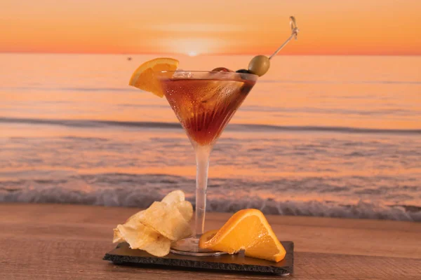 Cocktail com azeitonas, fatias de limão e batatas fritas com as ondas do mar no fundo — Fotografia de Stock