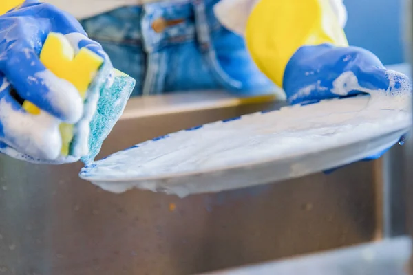 Pekerjaan rumah mencuci piring di wastafel dapur sarung tangan plastik biru dan kuning dengan banyak busa — Stok Foto