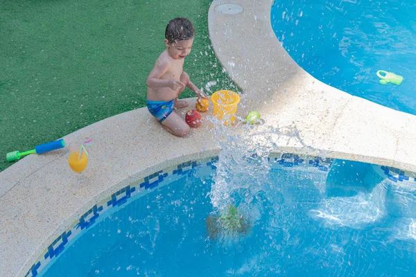 Le gamin s'amuse à éclabousser de l'eau pendant qu'il jette des fruits de saison pour l'été . — Photo