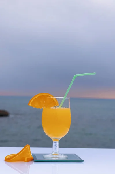 Close-up de um copo com delicioso suco de laranja e duas fatias de laranja madura e o fundo do mar - Laranja fresca e madura — Fotografia de Stock