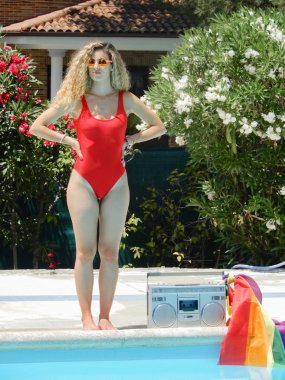 Güzel ve seksi kız mayo giymiş, gökkuşağı bayrağı ile büyük bir radyo yanında güneşleniyor