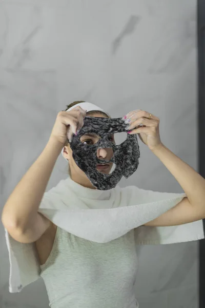 Молода жінка намагається на чорній бавовняній масці - сірий фон — стокове фото