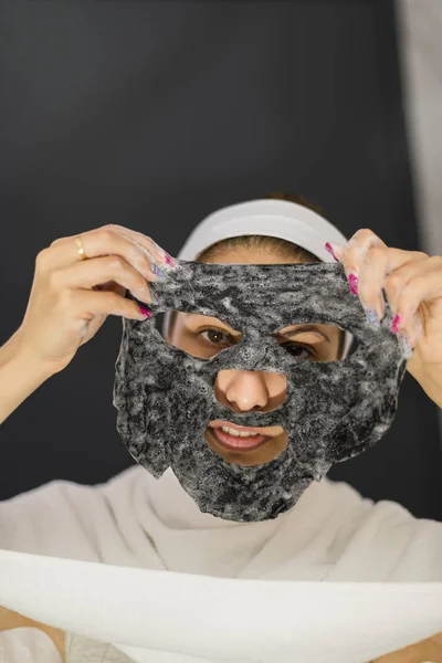Žena zobrazující svou černou bavlněnou masku-šedé pozadí — Stock fotografie