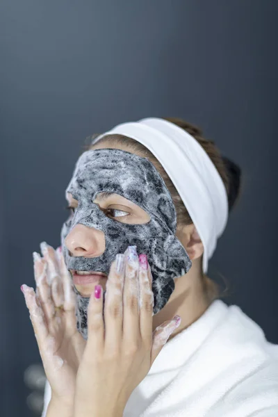 Portrét mladé ženy, která si na obličej aplikila černou masku-šedé pozadí — Stock fotografie