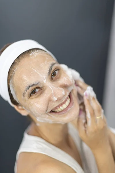 Pohled na krásnou, uvolněnou ženu, která si masírovala tvář bílou pěnou, aby vyčistila póry — Stock fotografie