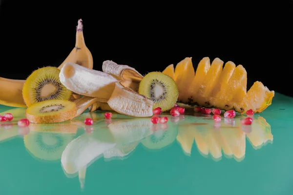 Delicious Hawaiian pineapple, banana, sliced green kiwi and red corn kernels on a green table and a black background