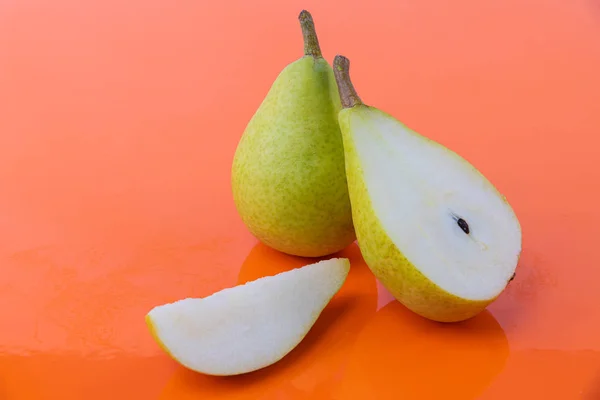 A pear cut in half, a piece and a whole pear - Sweet and ripe pear - Tasty wet pears on an orange background