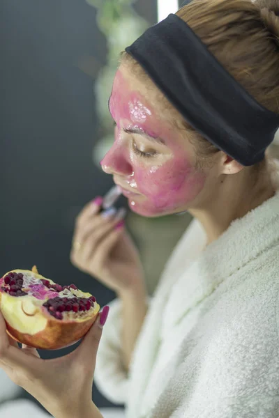 Деталь белой девушки, держащей гранат при нанесении маски на лицо - Organic Beauty Cosmetics — стоковое фото