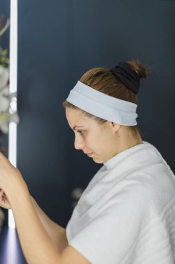 Kafasında atkı olan beyaz kadın siyah bir maske görüyor.