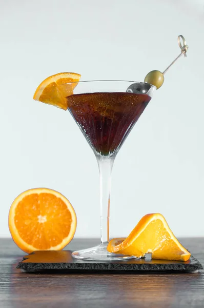Ciemny pomarańczowy napój w szklance. Kostki lodu i plasterki cytryny. Zielone i czarne oliwki. Wermut i gin. — Zdjęcie stockowe