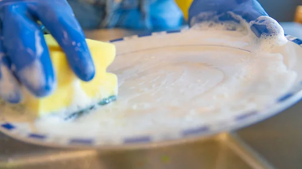 Primo piano delle mani con guanti e piatti di lavaggio spugne nel lavello della cucina — Foto Stock