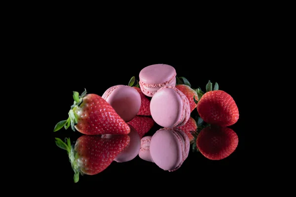 Fresas y deliciosos macarrones apilados en una mesa de vidrio con un fondo negro —  Fotos de Stock