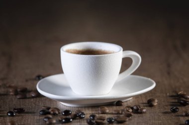 Ahşap bir masa üzerinde kahve tohumları ile çevrili beyaz bir kahve fincanı detay