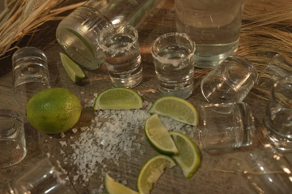 Vista superior de muchas rebanadas de lima fresca con sal espolvoreada por la mesa y tragos de tequila con una botella de tequila sobre la mesa — Foto de Stock