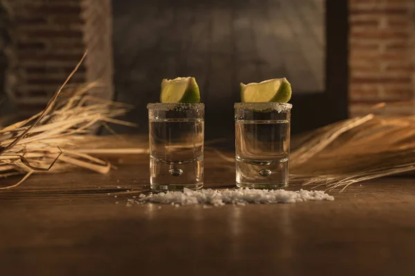 Dois deliciosos shots de tequila em uma mesa de madeira e buquês de palha no fundo — Fotografia de Stock