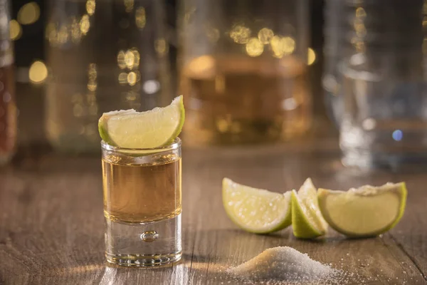 Lime szeleteket az asztalra, és ízletes lövés a Tequila a Tequila palackok az alján és a só elszórtan a fából készült asztal — Stock Fotó