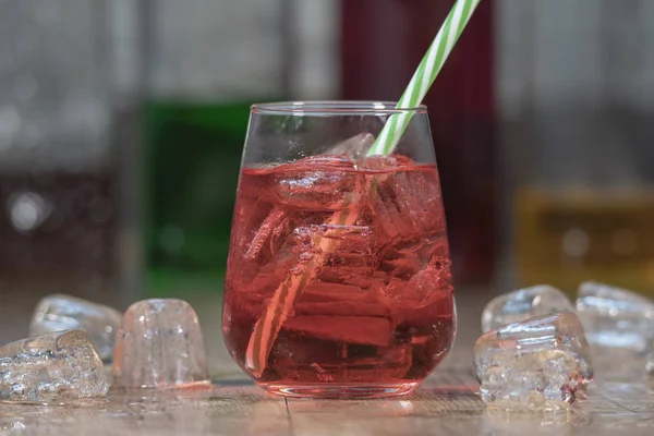 Czerwony napój z kostek lodu i słomy w szklance na drewnianym stole — Zdjęcie stockowe