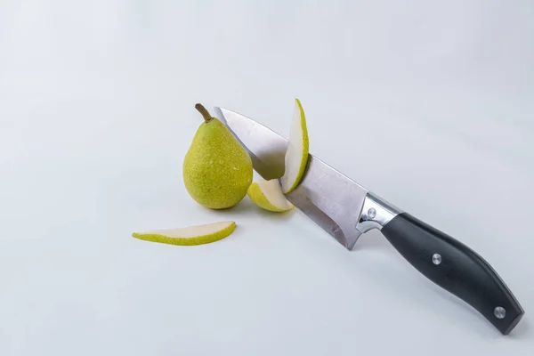 Ένα μαχαίρι με φέτες αχλάδι που συνοδεύεται από ένα ολόκληρο πράσινο αχλάδι σε λευκό φόντο-φρέσκα αχλάδια — Φωτογραφία Αρχείου