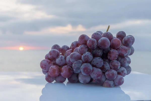 Suculento e delicioso bando de uvas roxas em uma mesa branca, com o sol no fundo — Fotografia de Stock