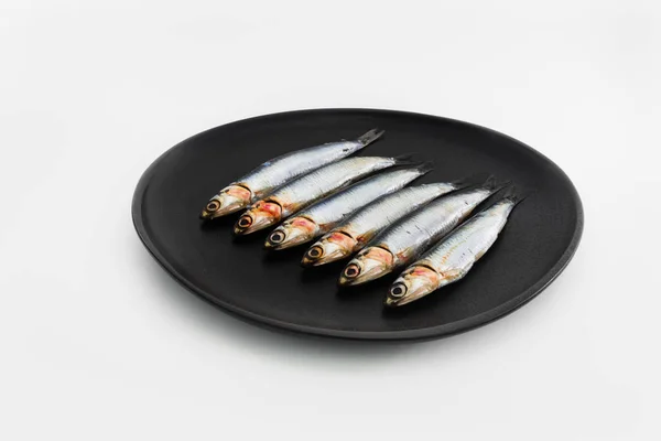 Färska sardiner på en svart tallrik på en vit bakgrund. Concept o — Stockfoto