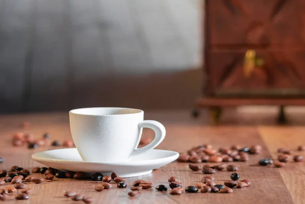 Foto-Detail vieler Kaffeebohnen rund um eine weiße Porzellantasse mit selektivem Fokus auf einem Holztisch. Konzept der Entspannung und des Kaffeearomas. — Stockfoto