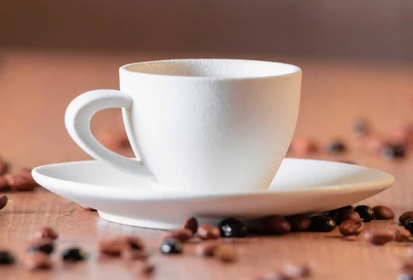 Eine weiße Tasse mit selektivem Fokus, umgeben von großen gerösteten Kaffeebohnen auf einem Holztisch. — Stockfoto