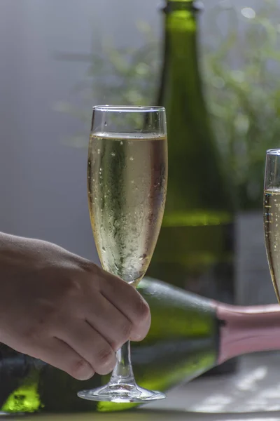 Close-up de uma mão tomando uma taça de champanhe em um casamento, duas garrafas verdes de champanhe e uma taça cheia na mesa branca . — Fotografia de Stock