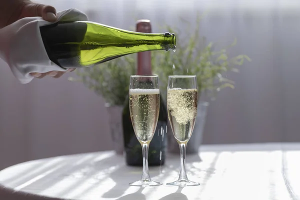 Uma mão segurando uma garrafa de cava enquanto enche um copo em um casamento. No fundo outra garrafa de cava e um vaso em uma mesa branca . — Fotografia de Stock