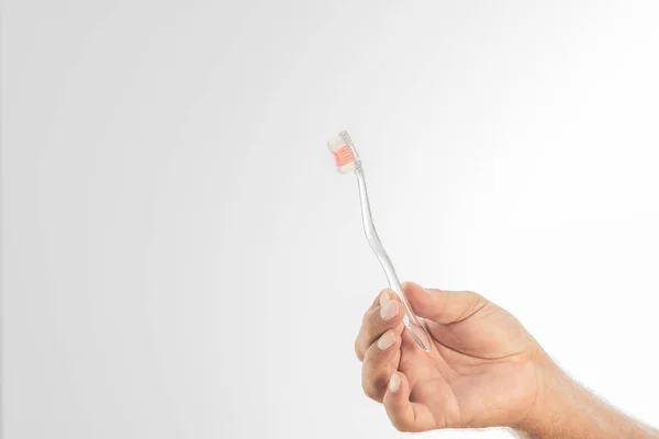 Uma escova de dentes de plástico transparente segurada pela mão de um homem sobre um fundo branco. Espaço para escrever . — Fotografia de Stock