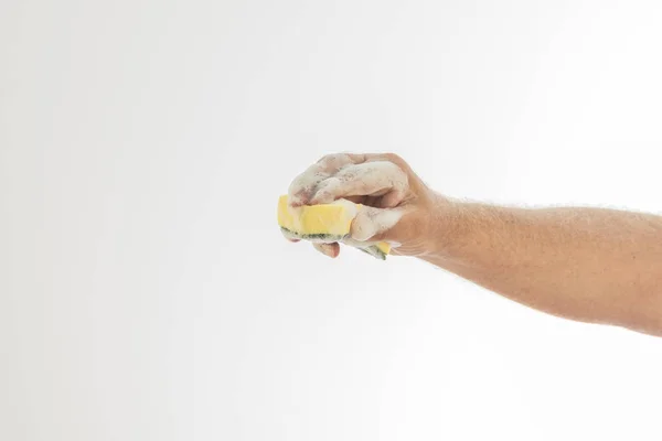 Une main d'homme pleine de mousse blanche tenant une éponge à vaisselle sur un fond blanc . — Photo