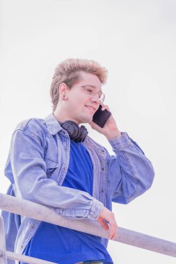 Yakışıklı sarışın çocuk telefonda konuşurken ve kahve şort ve mavi ceket ile mavi bir t-shirt giyen bir metal tüp elini eğilerek.