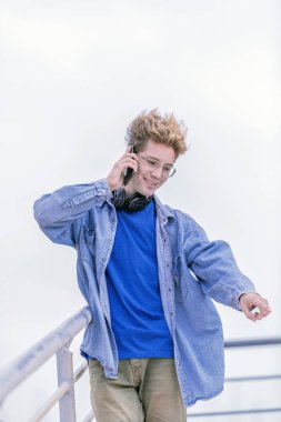 Pretty sarışın çocuk aşağı işaret ve telefonda konuşurken ve ihtiyatlı gülümseyerek aynı yöne bakıyor.