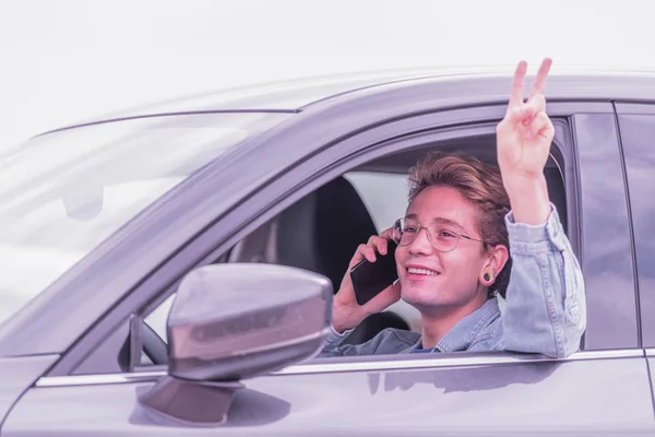 Blond chłopiec pozdrowienia w bardzo miły sposób siedząc w samochodzie rozmawia na telefon w okularach i kurtka. — Zdjęcie stockowe