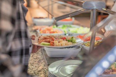 Yemek büfesinin penceresinin yanında bir kadının elinden tutulan karides ve sebzeli beyaz bir tabak. Gastronomik gıda kavramı.