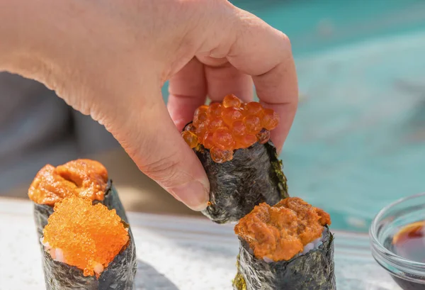 Mužská ruka, která položí kus sushi na jakési prkno na sekání jídla na stůl.. — Stock fotografie