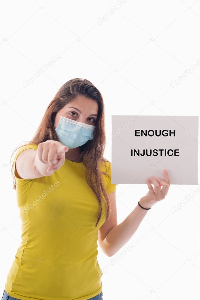 Young woman using a surgical mask holding a sign with a message and pointing at the camera on a light background. Racism and awareness concept.