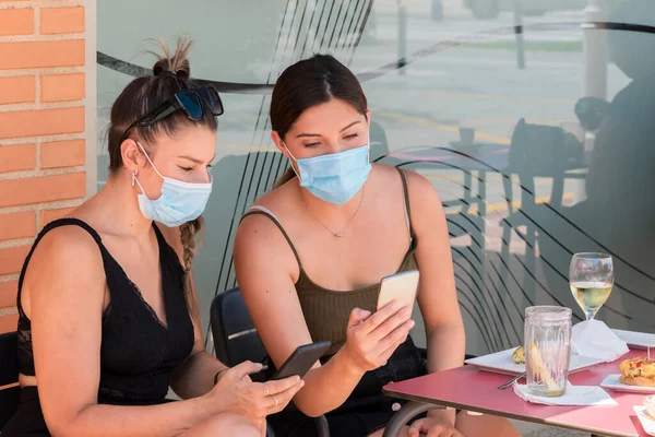 Dos Mujeres Con Máscaras Quirúrgicas Revisando Sus Teléfonos Juntas Mientras — Foto de Stock
