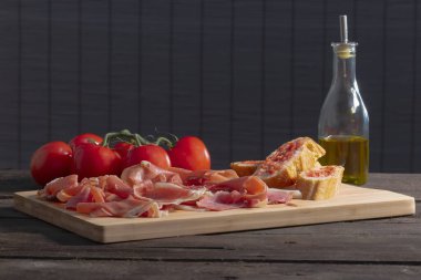 İnce dilimler halinde İspanyol jambonu, domatesli ekmek, taze domates ve odaklı olmayan bir arka plan üzerinde zeytin yağı bulunan cam bir şişe. Geleneksel gıda ve lezzet kavramı.