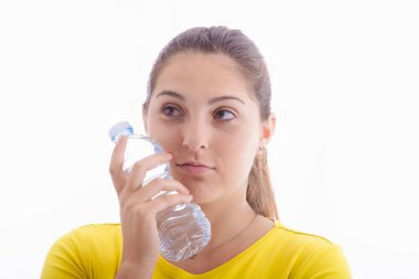 Derin düşüncelere dalmış güzel bir genç kadının hafif bir arka planda yanağına bir şişe su tutmasına yakından bakın. Sağlıklı yaşam tarzı kavramı.