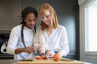 Gülümseyen güzel bir kadın yakışıklı bir siyahla domates kesiyor ve arka planda odak noktasını işaret ediyor. Çiftler ve çeşitlilik kavramı.