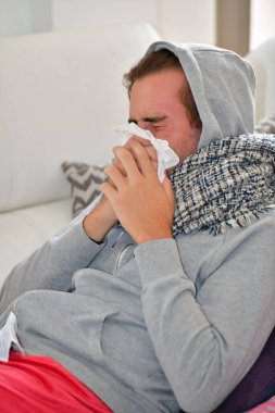 Kapüşonlu bir genç adam ve kağıt peçeteyle burnunu silen bir eşarp. Hastalık ve hijyen kavramı.