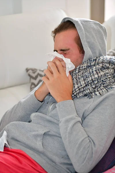 Kapüşonlu bir genç adam ve kağıt peçeteyle burnunu silen bir eşarp. Hastalık ve hijyen kavramı.