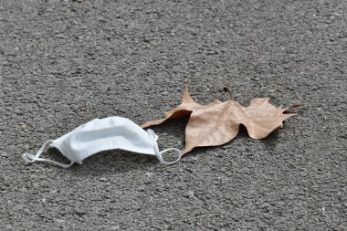 Asfalttaki kuru yaprağın yanında kullanılmış bir cerrahi maske.