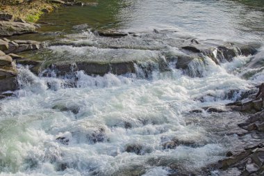 Kayalar ile açık nehir dağlara doğru küçük şelale yol açar..