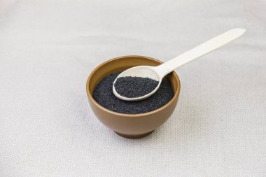 Bir ışık çuval bezi arka plan üzerine bir tahta kaşıkla bir tabak içinde siyah kimyon.