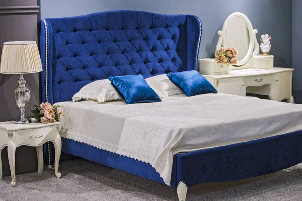 Luxury royal bedroom in antique style with blue velvet bed and white nightstand.